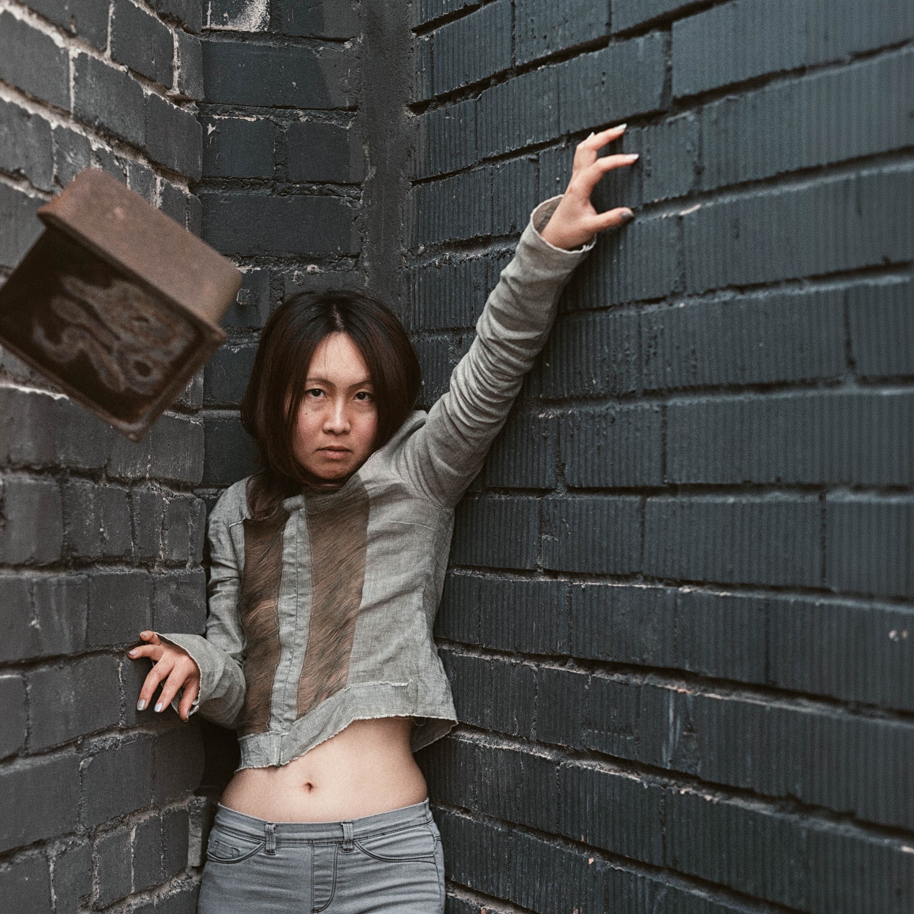 Lily-Yuri against dark brickwork in Tallinn, wearing a distressed linen top