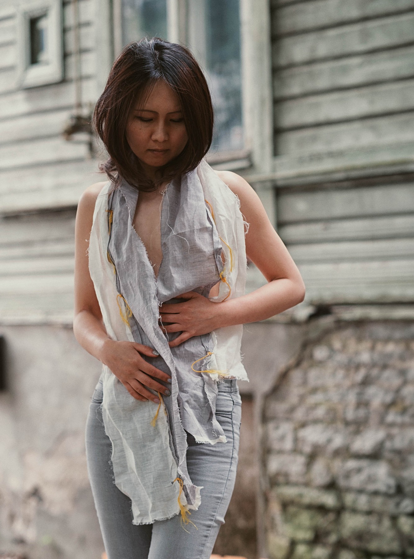 Lily-Yuri adjusting a handmade linen garment outside a wooden building in Tallinn